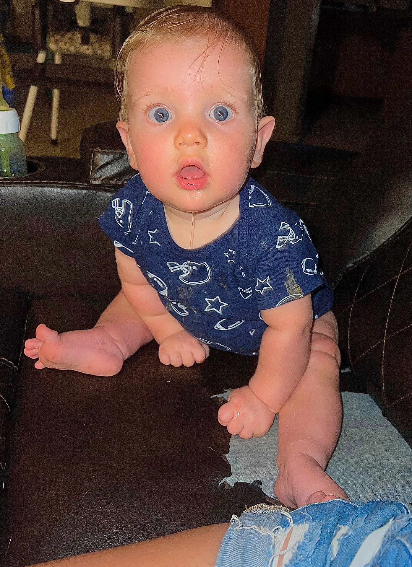 Sebastian is registered to the contest to win money with this photo: baby, child, infant, dribble, blue_eyes, onesie, sitting, leather_couch, indoor, curious, wide_eyes, clothing, foot, hand, face, expression, young, furniture, home, casual
