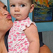 Ryland is registered to the contest to win money with this photo: baby, child, adult, face, person, kissing, flamingo_pattern, clothing, arm, painting, wall, indoor, expression, curious, skin, holding, colorful, furniture, portrait, closeup