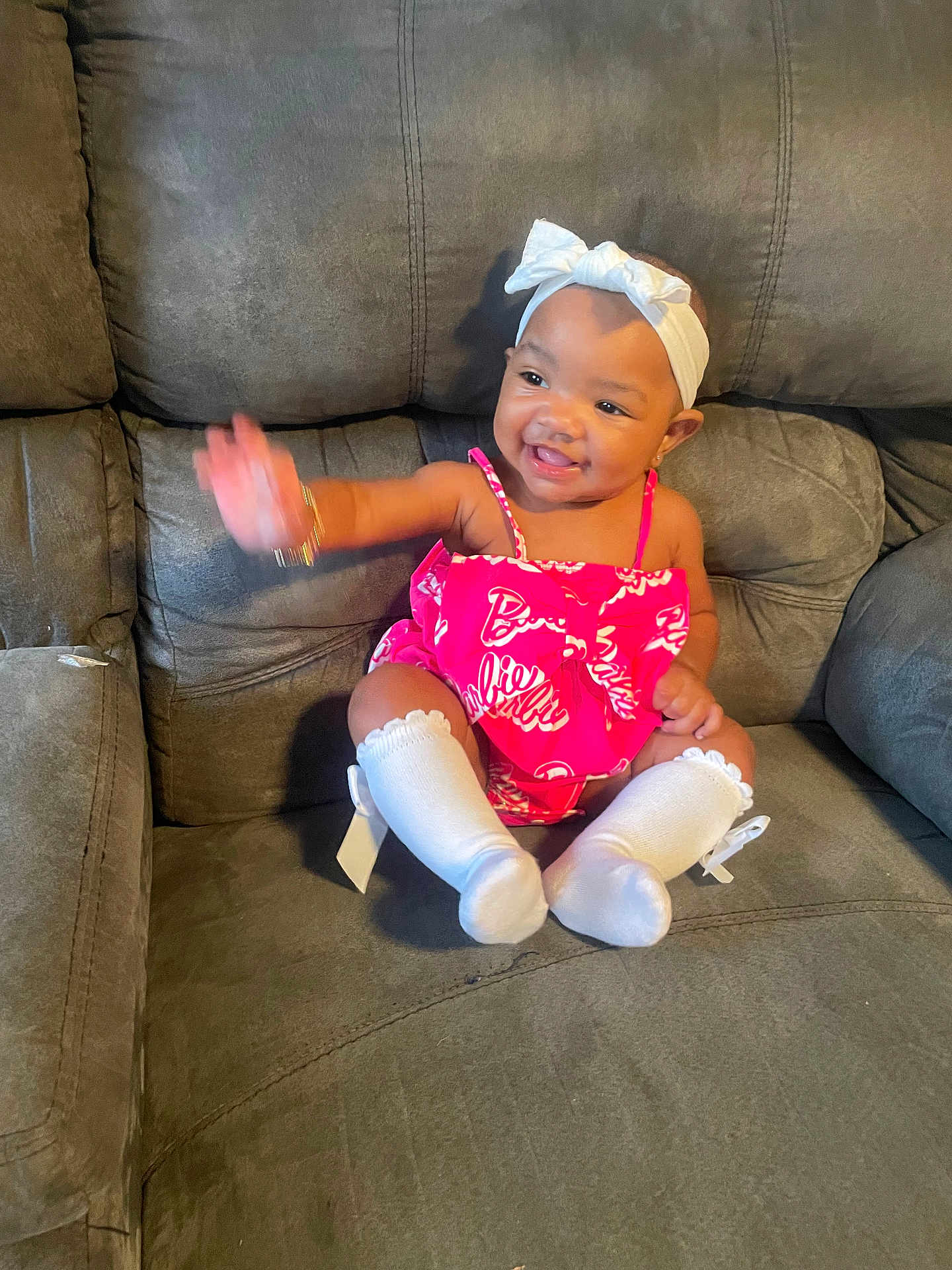 Malani joined the competition — help win amazing prizes! baby, child, smiling, waving, pink_outfit, white_socks, headband, couch, indoor, happy, sitting, cute, person, infant, fashion, accessory, furniture, portrait, joyful, casual
