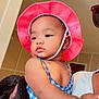 baby, child, pink_hat, blue_outfit, earring, indoor, person, adult_hand, holding, portrait, cute, chubby_cheeks, contemplative, clothing, skin, face, headwear, sleeveless, fashion, human