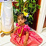 adult, bright_colors, child, cultural, curious, decor, feet, flower_hair_accessory, girl, home, indoor, jewelry, person, plant, portrait, sitting, tile_floor, traditional_dress, wooden_door, young