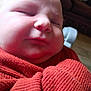 baby, closeup, face, sleeping, red_clothing, blanket, infant, soft_skin, cozy, child, portrait, peaceful, indoors, warm_lighting, knit, cute, young_child, resting, small_face, health