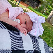 Addison joined the competition — help win amazing prizes! baby, newborn, pacifier, pink_clothing, bow_hat, blanket, black_and_white, checkered, outdoor, grass, tree, nature, infant, relaxing, headwear, portrait, child, peaceful, lying_down, summer