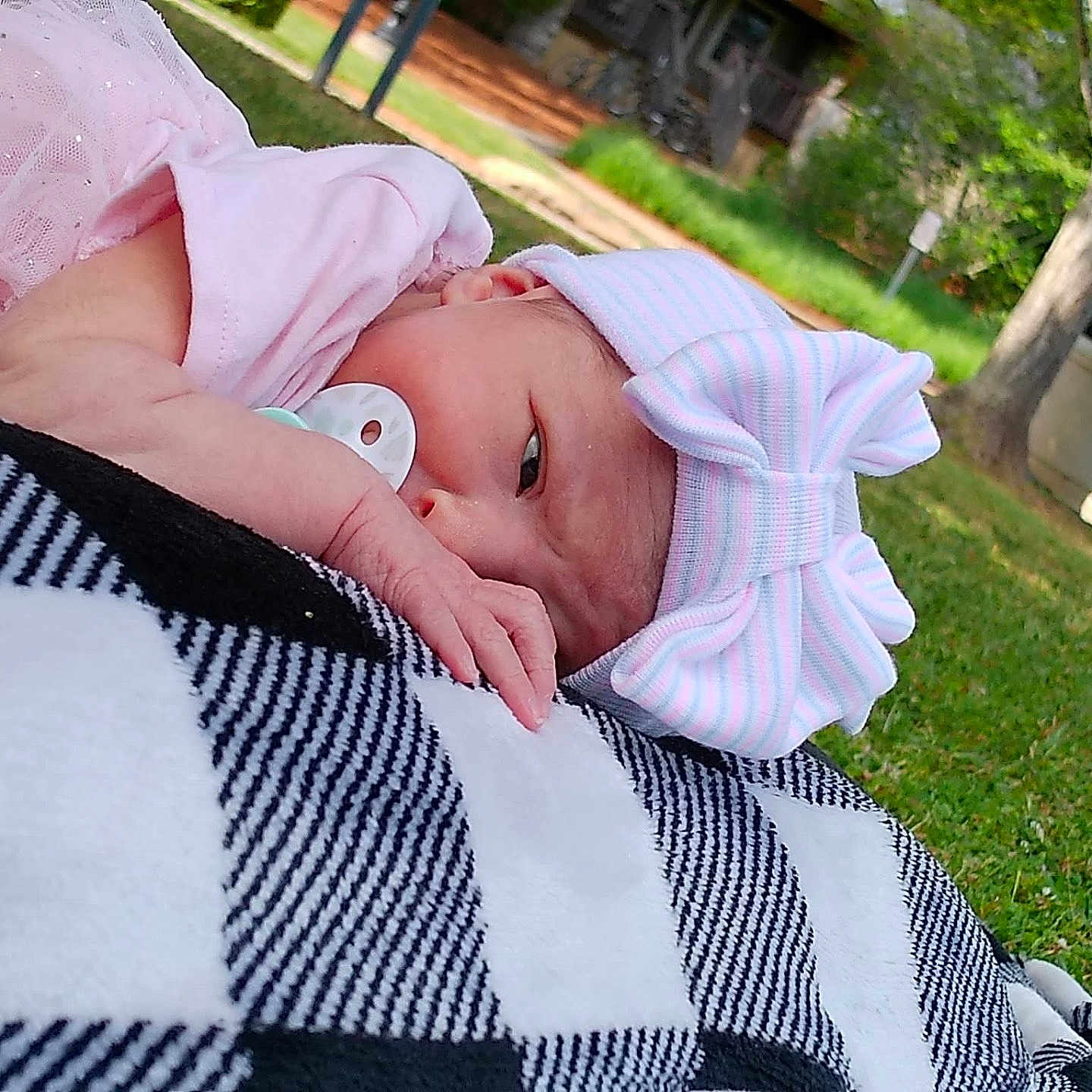 Addison joined the competition — help win amazing prizes! baby, newborn, pacifier, pink_clothing, bow_hat, blanket, black_and_white, checkered, outdoor, grass, tree, nature, infant, relaxing, headwear, portrait, child, peaceful, lying_down, summer