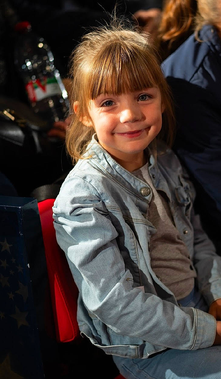 Lea participe au concours pour gagner de l'argent avec cette photo : automotive_lighting, bangs, blond, brown_hair, child, event, face, fun, hairstyle, happy, head, joy, luxury_vehicle, person, portrait_photography, sitting, sleeve, smile, toddler, tree