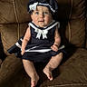 baby, child, sailor_outfit, blue_eyes, bow, hat, dress, sitting, couch, leather, brown, indoors, cute, portrait, infant, person, apparel, fashion, smile, soft_lighting