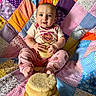 baby, child, cookie, snack, colorful_quilt, patchwork, sitting, pink_clothing, cute, happy, blue_eyes, indoor, food, stack, playful, infant, hand, foot, smile, portrait