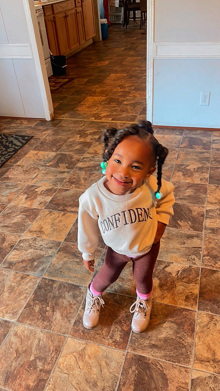 Alaiyah is registered to the contest to win money with this photo: baby_toddler_clothing, cabinetry, floor, flooring, happy, hardwood, human_leg, joint, joy, knee, leg, leisure, person, shoe, smile, sneakers, standing, thigh, toddler, white