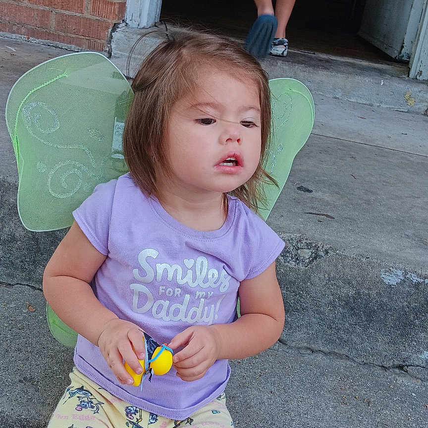 Aliveah is registered to the contest to win money with this photo: back_view, barefoot, brick_wall, cardboard_box, casual_clothing, child, concrete, doorway, fairy_wings, footwear, outdoor, pants, person, playing, purple_shirt, shorts, summer, toddler, toy, young_child