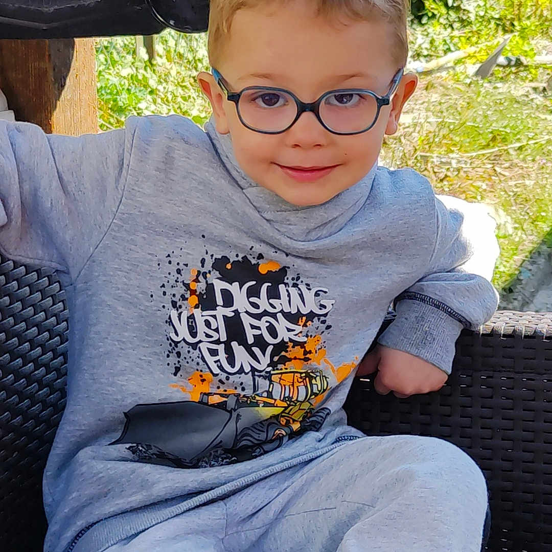 Ylliano a rejoint le concours — aidez-le/la à gagner de superbes lots ! casual, chair, child, comfort, daylight, fashion, footwear, glasses, gray_clothing, greenery, happy, outdoor, playful_text, portrait, relaxed, sitting, smiling, sweatshirt, woven_chair, young_boy