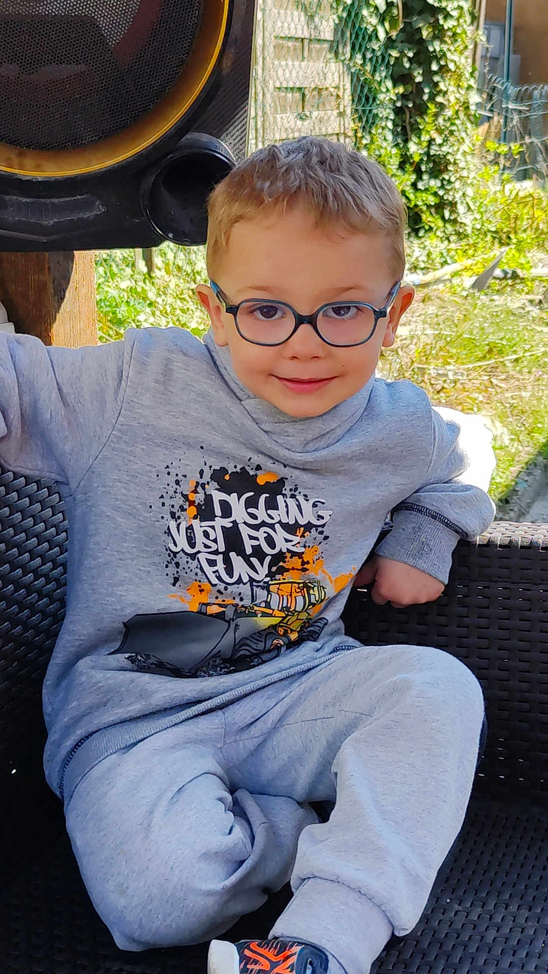 Ylliano a rejoint le concours — aidez-le/la à gagner de superbes lots ! child, glasses, sweatshirt, gray_clothing, sitting, chair, outdoor, greenery, smiling, casual, footwear, playful_text, young_boy, comfort, daylight, portrait, relaxed, woven_chair, fashion, happy