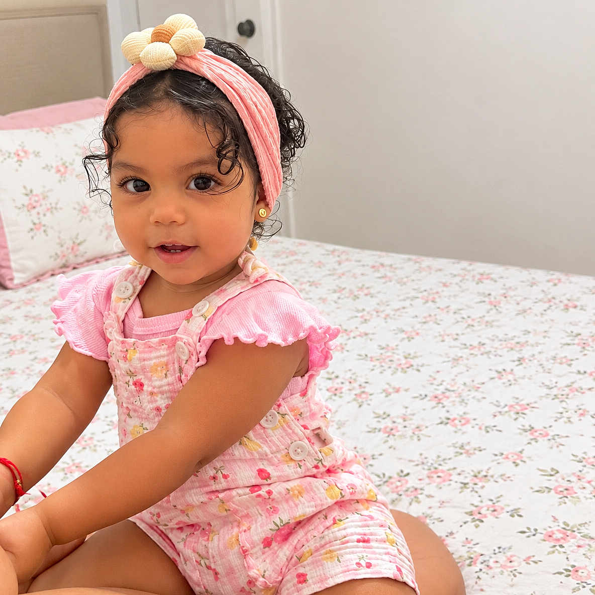 Caroline is registered to the contest to win money with this photo: child, toddler, girl, portrait, smiling, sitting, bedroom, bed, floral, pink_clothing, headband, curly_hair, earrings, baby, indoors, home, face, fashion, happy, photography