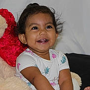 Caroline is registered to the contest to win money with this photo: child, toddler, girl, smiling, sitting, portrait, indoor, bed, blanket, stuffed_animal, plush_toy, white_shirt, floral_pattern, barefoot, hair_bow, earrings, bracelet, happy, cozy, photography