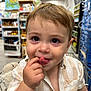aisle, baby, child, clothing, curious, cute, face, finger_in_mouth, fun, indoor, person, playful, retail, shopping_cart, short_hair, smiling, striped_shirt, supermarket, toddler, young_child