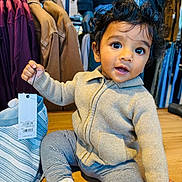 Prabhu joined the competition — help win amazing prizes! baby, casual_wear, child, clothing_tag, curious_expression, curly_hair, cute, hangers, holding, indoor, jackets, person, retail, shopping, socks, store, striped_pants, sweater, toddler, wooden_floor