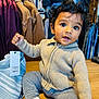 toddler, child, curly_hair, sweater, striped_pants, socks, clothing_tag, shopping, store, jackets, hangers, wooden_floor, curious_expression, indoor, person, holding, casual_wear, cute, retail, baby