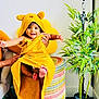 baby, child, towel, yellow, smile, happy, face, feet, hands, woven_basket, plant, potted_plant, indoor, person, hooded_towel, colorful, furniture, room, joyful, cute