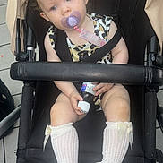 Nala joined the competition — help win amazing prizes! toddler, child, stroller, pacifier, bow, leopard_print, socks, white_shoes, baby_bottle, curious, indoors, floor_tiles, seat_belt, black_stroller, clothing, person, baby, cute, sitting, holding