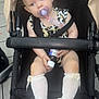 toddler, child, stroller, pacifier, bow, leopard_print, socks, white_shoes, baby_bottle, curious, indoors, floor_tiles, seat_belt, black_stroller, clothing, person, baby, cute, sitting, holding