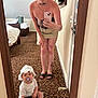 woman, toddler, mirror, selfie, carpet, bedroom, pacifier, blanket, remote_control, white_bonnet, tattoos, glasses, phone, carpeted_floor, door, bed, table, clothing, indoor, person