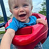 child, toddler, smiling, swing, playground, outdoor, blue_shirt, red_swing, happy, person, shorts, daylight, park, grass, trees, play, fun, cute, baby, summer