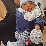 Osiah is registered to the contest to win money with this photo: baby, infant, pacifier, blue_hat, striped_pants, mittens, dinosaur_pattern, adult_hand, pink_nails, indoor, person, clothing, holding, closeup, cute, newborn, child, face, socks, comfort