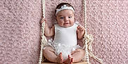 Eïlynn participe au concours pour gagner de l'argent avec cette photo : baby, infant, swing, white_clothing, headband, cute, smiling, pink_background, rope, wooden_swing, texture, soft, portrait, child, happy, sitting, indoors, toddler, flower_decor, hands