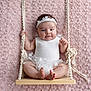 baby, infant, swing, white_clothing, headband, cute, smiling, pink_background, rope, wooden_swing, texture, soft, portrait, child, happy, sitting, indoors, toddler, flower_decor, hands