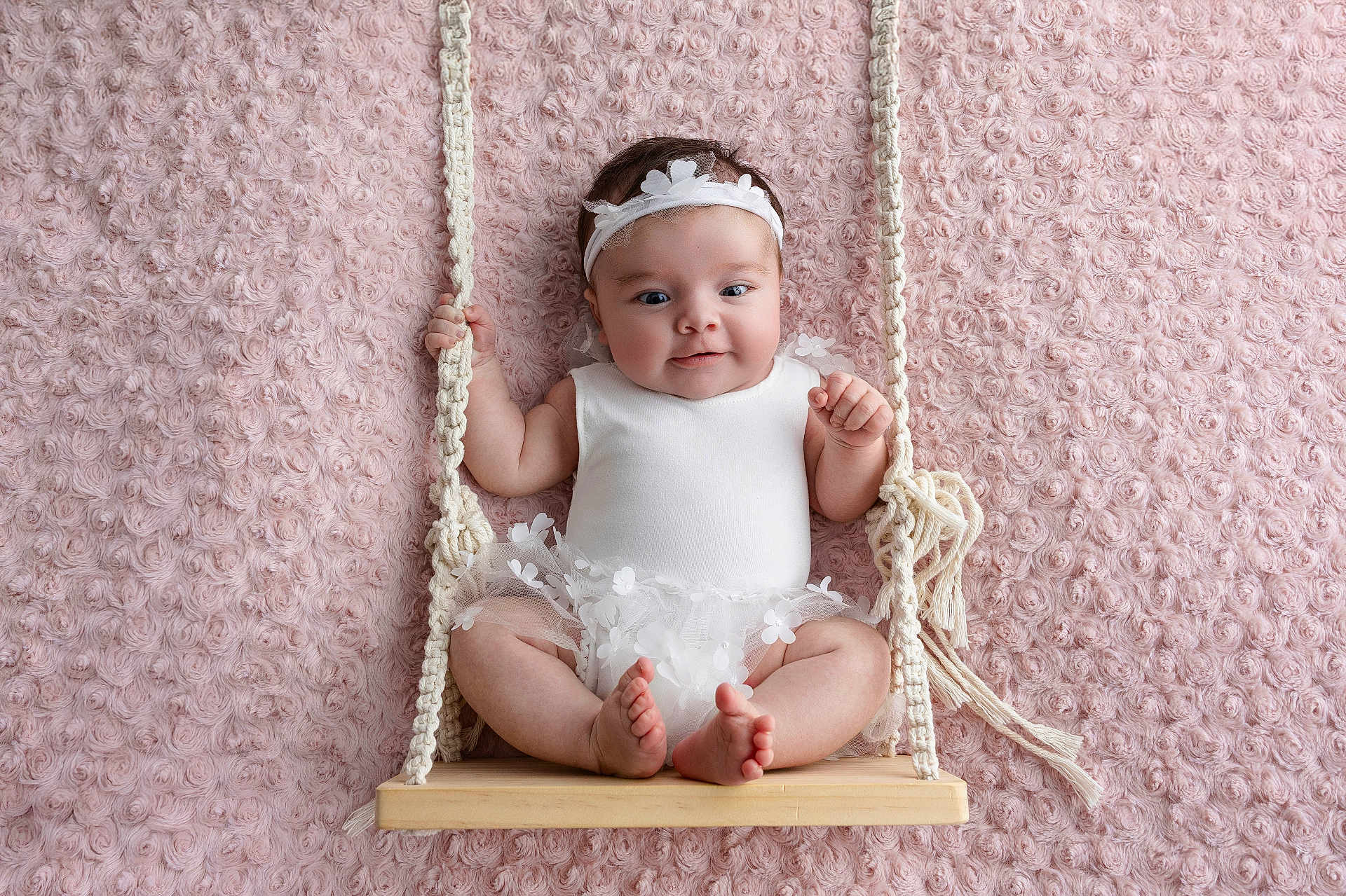 Eïlynn participe au concours pour gagner de l'argent avec cette photo : baby, infant, swing, white_clothing, headband, cute, smiling, pink_background, rope, wooden_swing, texture, soft, portrait, child, happy, sitting, indoors, toddler, flower_decor, hands