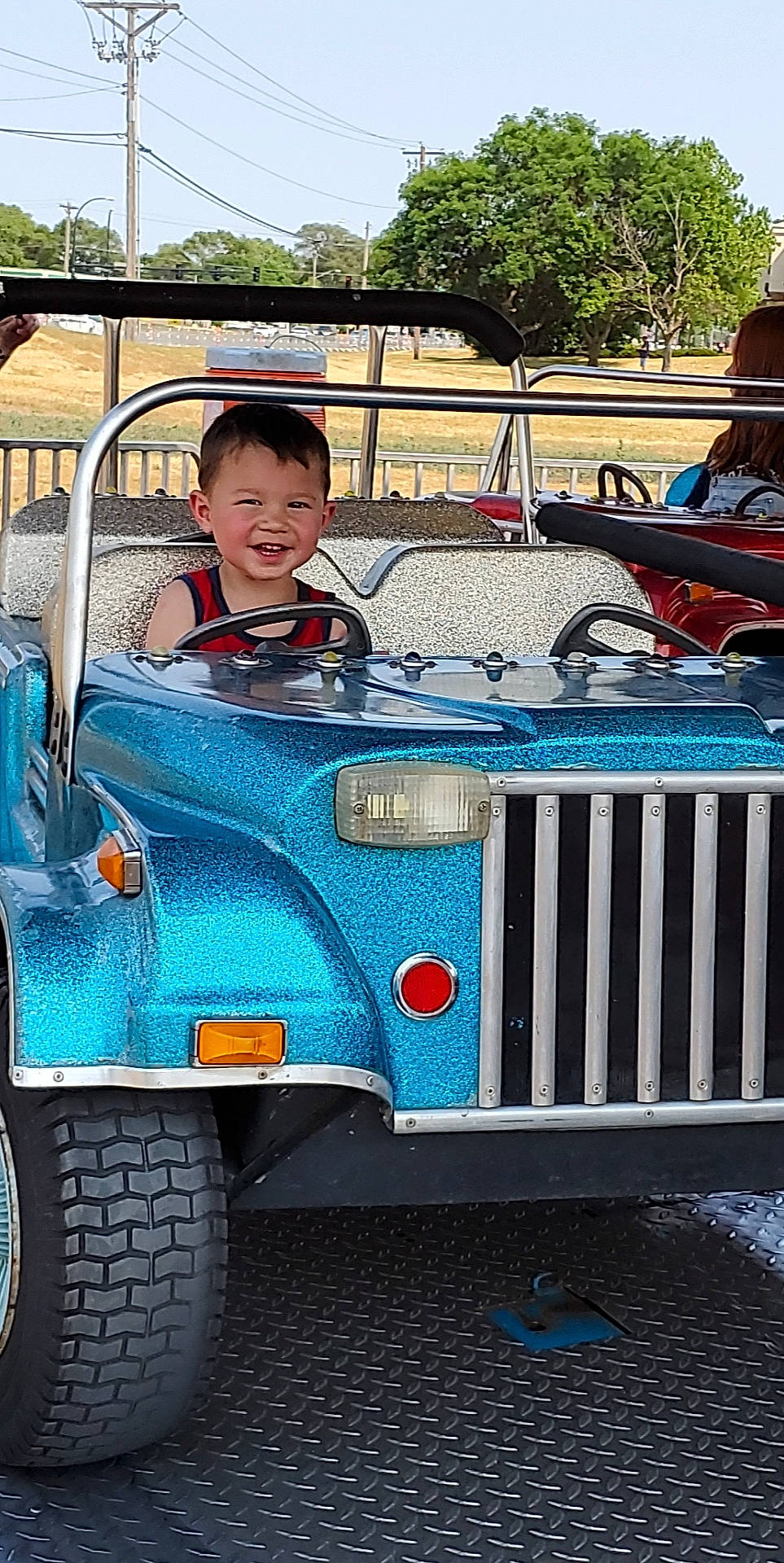 Grayson is registered to the contest to win money with this photo: automotive_design, automotive_exterior, automotive_tire, automotive_wheel_system, bumper, car, fender, grille, hood, joy, land_vehicle, mode_of_transport, motor_vehicle, person, sky, smile, tire, tread, tree, vehicle