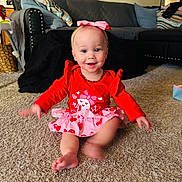 Ember is registered to the contest to win money with this photo: baby, toddler, child, sitting, smile, red_dress, heart_pattern, pink_bow, headband, necklace, carpet, living_room, couch, throw_blanket, decorative_pillows, toy, baby_seat, barefoot, motion_blur, portrait
