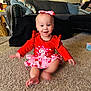 baby, toddler, child, sitting, smile, red_dress, heart_pattern, pink_bow, headband, necklace, carpet, living_room, couch, throw_blanket, decorative_pillows, toy, baby_seat, barefoot, motion_blur, portrait