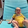 baby, child, smiling, yellow_onesie, outdoor, lounge_chair, sunlight, happy, infant, diaper, blue_chair, concrete, brick_wall, hand, legs, casual, summer, relaxing, cute, portrait