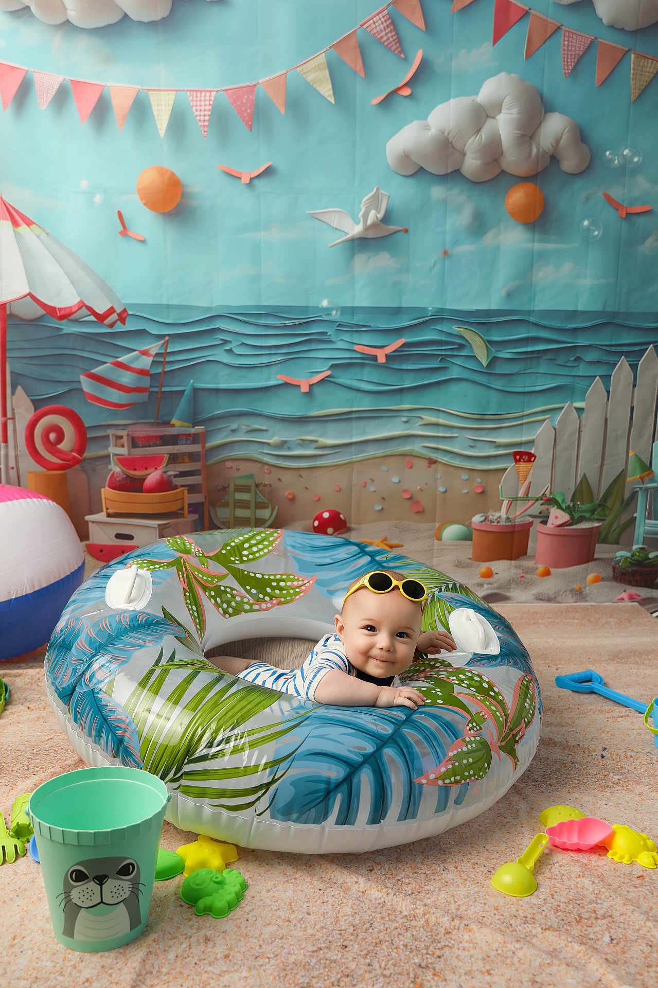Kris participe au concours pour gagner de l'argent avec cette photo : baby, sunglasses, inflatable_ring, beach_toys, sand, toys, indoor, playtime, child, smiling, colorful, background, decorations, bucket, shovel, mushroom, beach_ball, umbrella, picket_fence, play_area