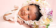 Vivianna joined the competition — help win amazing prizes! baby, infant, flower_crown, floral_bonnet, pink_background, portrait, newborn, cute, soft_lighting, face, headwear, smile, child, resting, adorable, skin, hand, closeup, young, peaceful