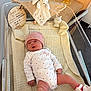 baby, baby_clothes, baby_girl, bassinet, blanket, cute_expression, face, hospital, hospital_band, indoor, infant, knitted_blanket, lying_down, newborn, onesie, person, pink_hat, soft_toy, toy, wooden_plaque
