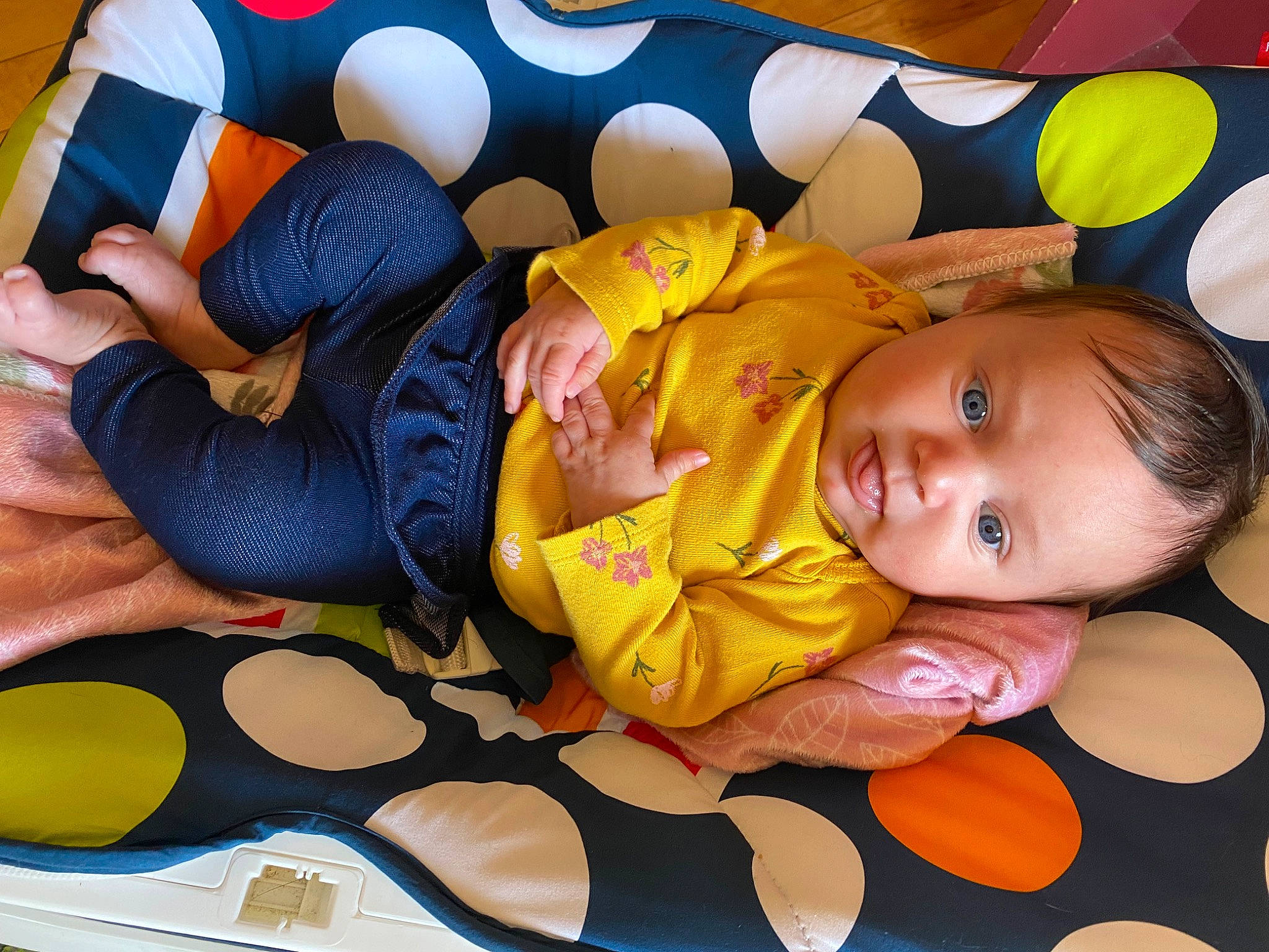 Lucille is registered to the contest to win money with this photo: baby, baby_products, baby_toddler_clothing, child, comfort, facial_expression, finger, flooring, fun, happy, head, linens, orange, pattern, person, room, sitting, textile, toddler, wood