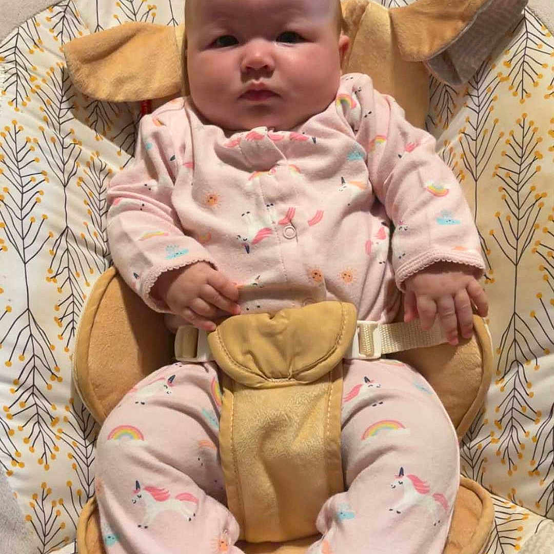 Raina joined the competition — help win amazing prizes! baby, infant, child, sitting, bouncer, baby_seat, pink_outfit, unicorn, socks, smiling_socks, face, portrait, indoors, cushion, blanket, patterned_fabric, harness, furniture, cozy, photograph