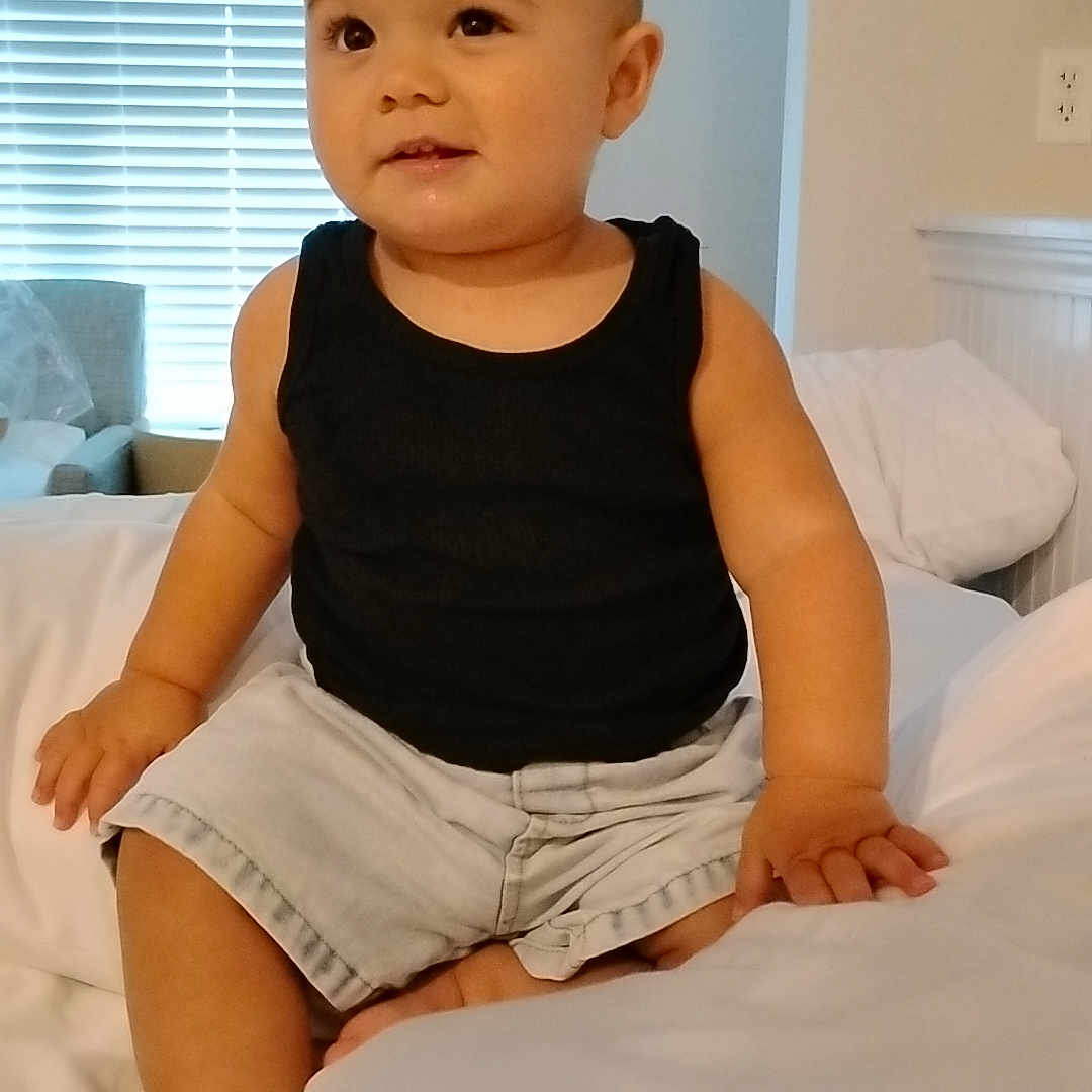 Ascension joined the competition — help win amazing prizes! toddler, child, baby, portrait, sitting, bed, bedroom, black_tank_top, shorts, smiling, face, person, indoors, home, window, blinds, pillow, bedding, furniture, daylight