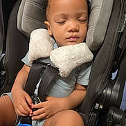 Miles is registered to the contest to win money with this photo: toddler, child, car_seat, sleeping, safety_harness, toy, hands, clothing, shorts, shirt, curly_hair, indoors, seat, resting, peaceful, baby, travel, car_interior, infant, cute