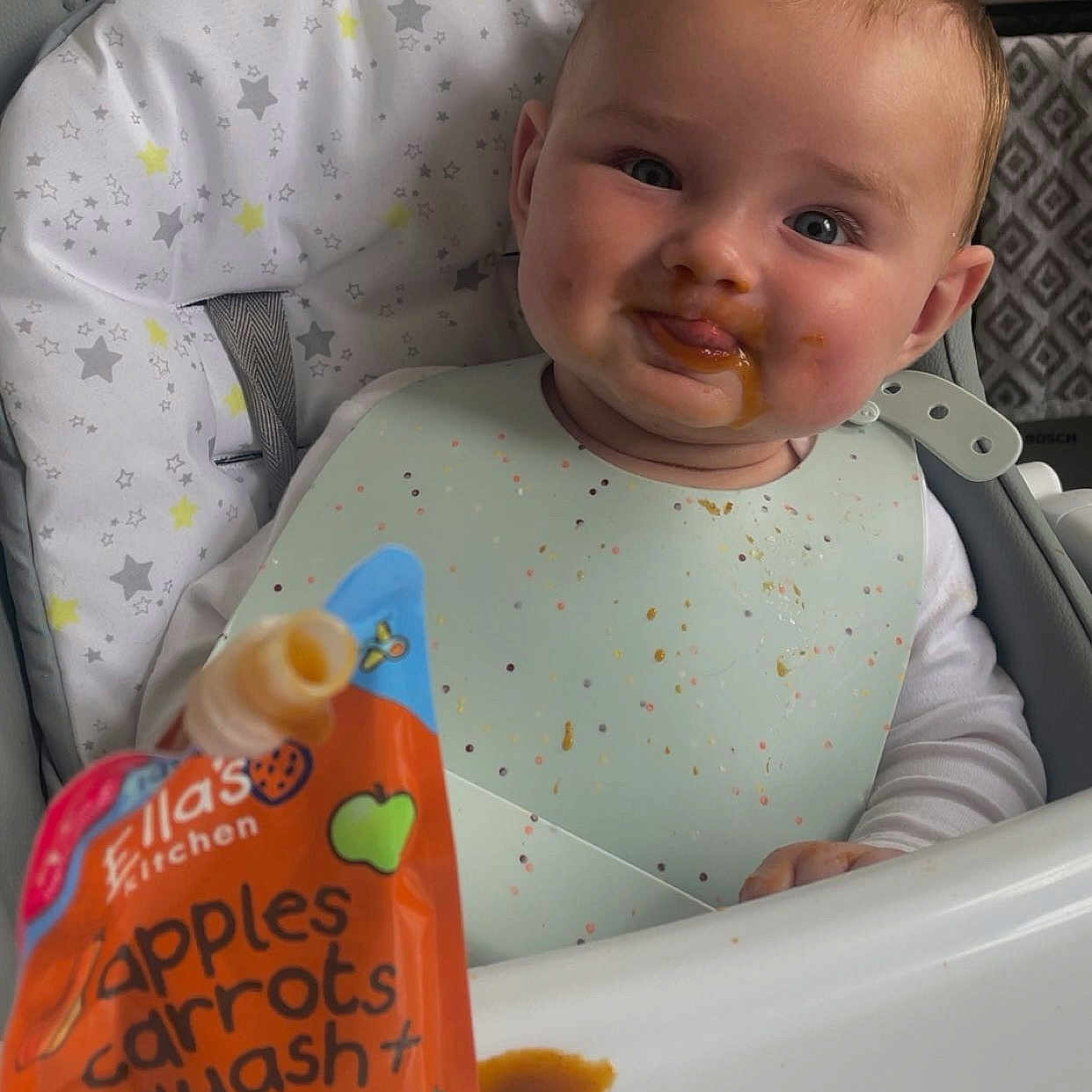 Arron is registered to the contest to win money with this photo: baby, bib, child, clothing, container, expression, face, feeding, food, hand, high_chair, indoor, infant, kitchen, messy, organic_food, plate, seat, smile, table