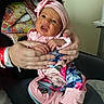Serenity joined the competition — help win amazing prizes! baby, infant, child, portrait, smiling, pink_headband, floral_outfit, colorful_clothing, being_held, adult_hands, face, eyes, mouth, indoor, seated, blanket, chair, family, photography, adorable