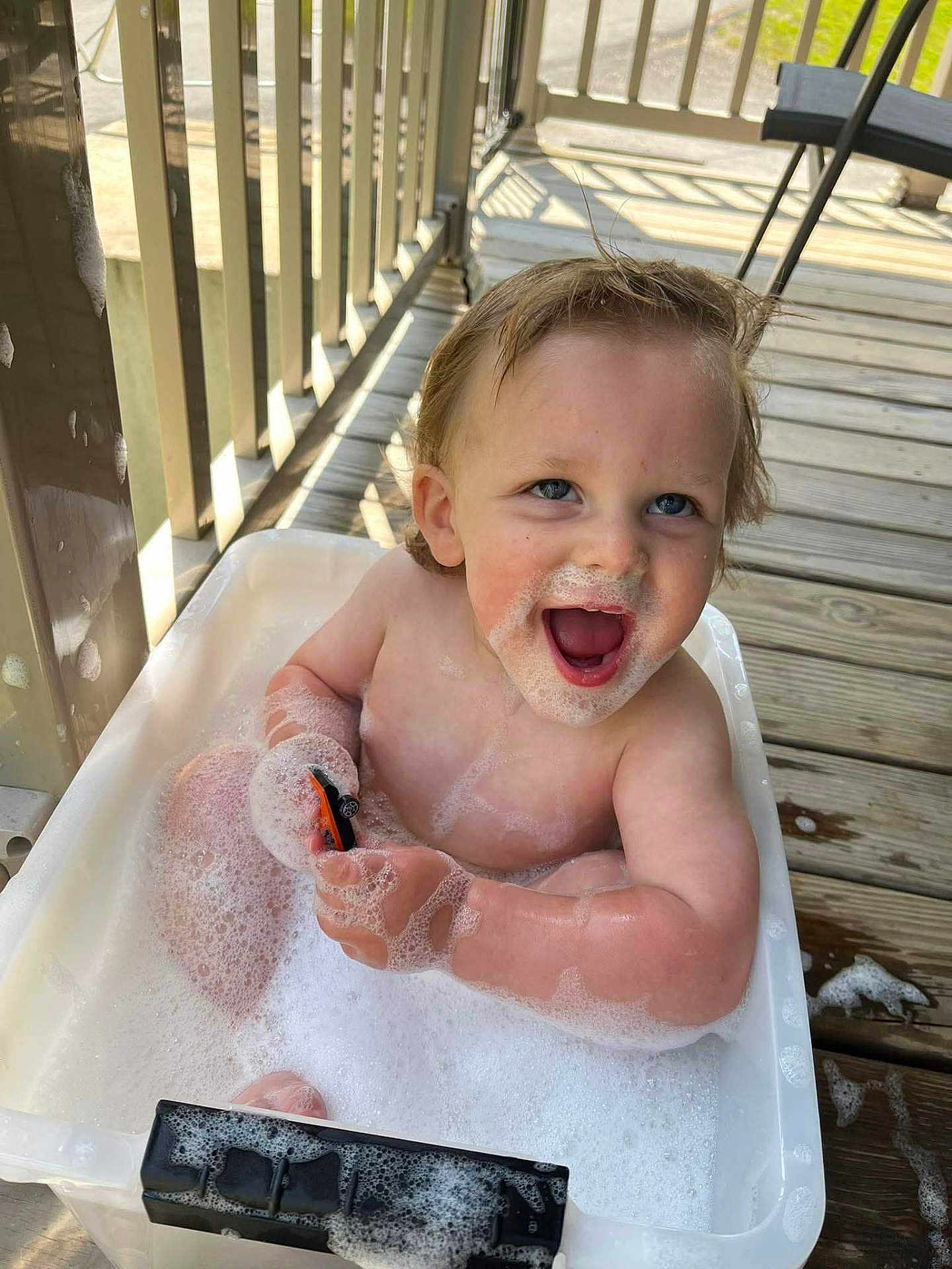 Adrian joined the competition — help win amazing prizes! toddler, child, bath, bubbles, soap, toy_car, smile, happy, water, foam, outdoor, porch, wooden_floor, sunlight, play, cute, face, hands, skin, hair