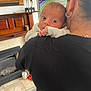 Ruben is registered to the contest to win money with this photo: baby, infant, person, adult, shoulder, earring, living_room, fireplace, television, tennis, giraffe_statue, floor_tiles, carpet, black_shirt, hand, face, eyes, curious, indoor, holding