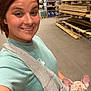 Lucey is registered to the contest to win money with this photo: woman, selfie, dog, puppy, french_bulldog, sling_pouch, warehouse, lumber, wood, smiling, casual_clothing, short_hair, indoor, curious, pet, animal, person, blue_eyes, cute, friendly