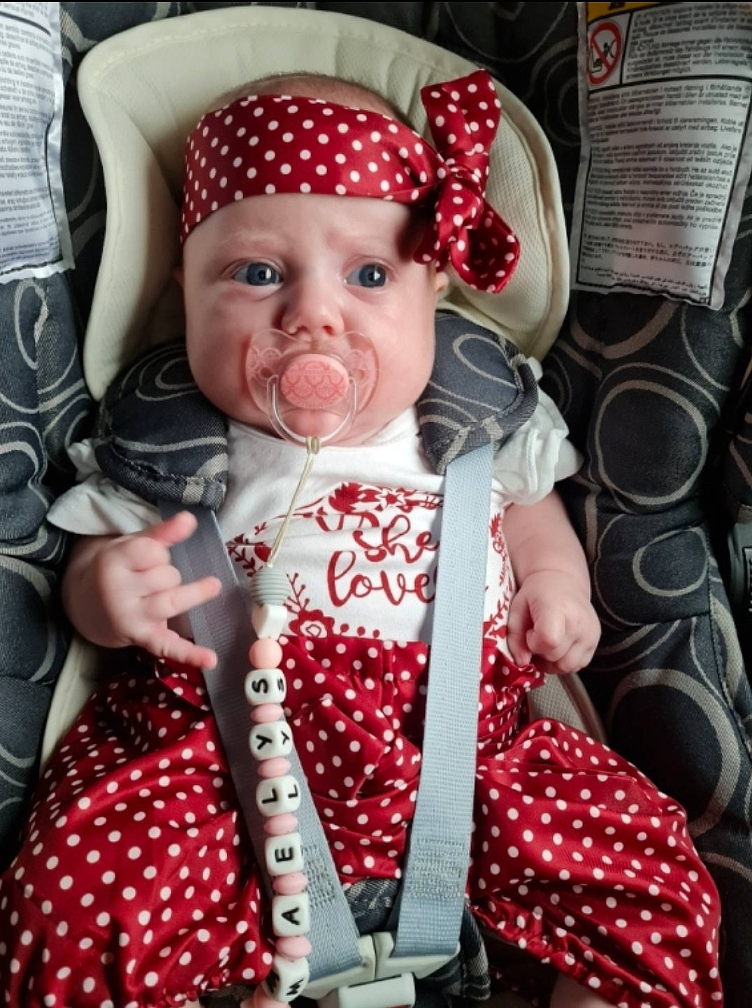 Maëlys a rejoint le concours — aidez-le/la à gagner de superbes lots ! baby, baby_carriage, baby_products, baby_toddler_clothing, cap, cheek, child, costume_hat, dress, fashion_accessory, fun, happy, headwear, pattern, peach, person, pink, plaid, polka_dot, sitting