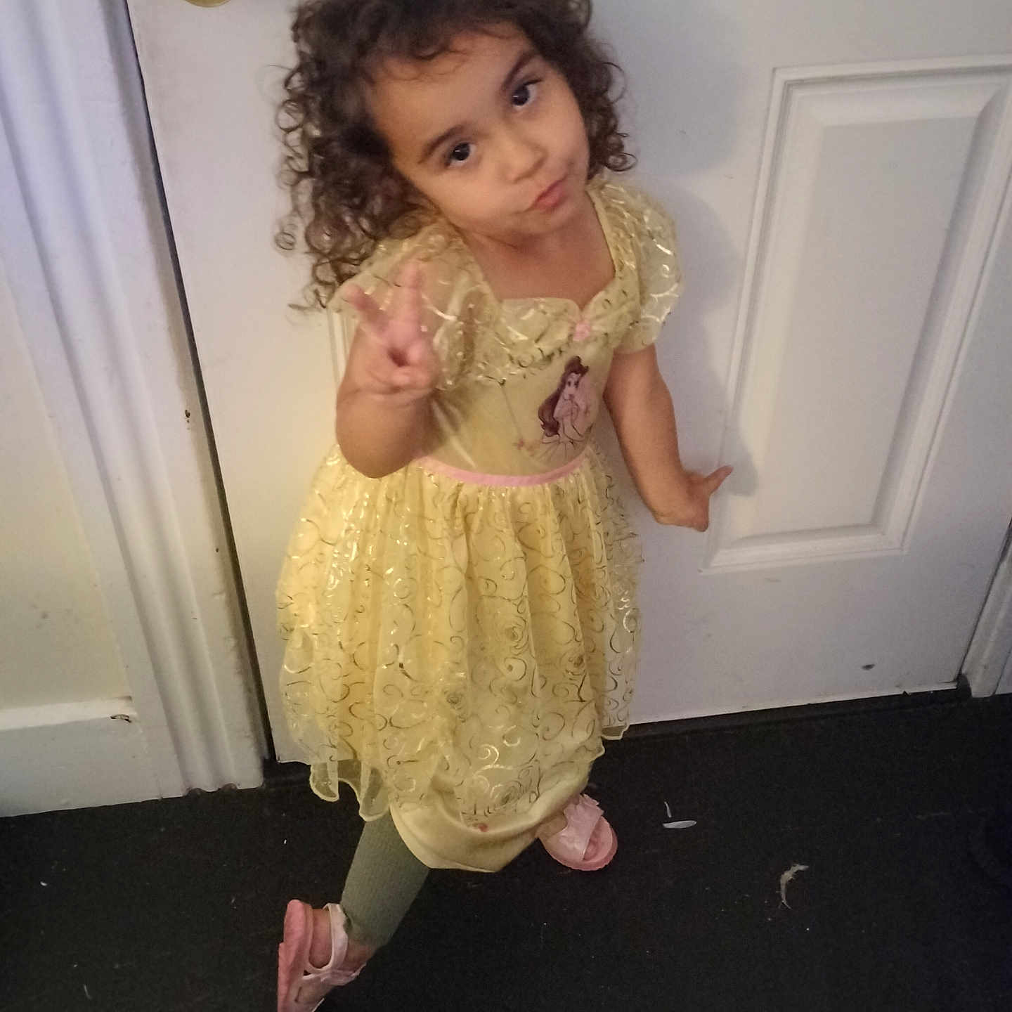 Novalie joined the competition — help win amazing prizes! carpet, child, clothing, curly_hair, door, expression, floor, footwear, girl, green_leggings, indoor, peace_sign, person, pink_sandals, playful, pose, princess_dress, yellow_dress, young