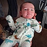 Exton is registered to the contest to win money with this photo: adult_arm, baby, being_held, chair, child, clothing, dinosaur_pattern, face, home, indoor, infant, onesie, photography, portrait, serious_expression, sitting, smartphone_text, stroller, tattoo, walker