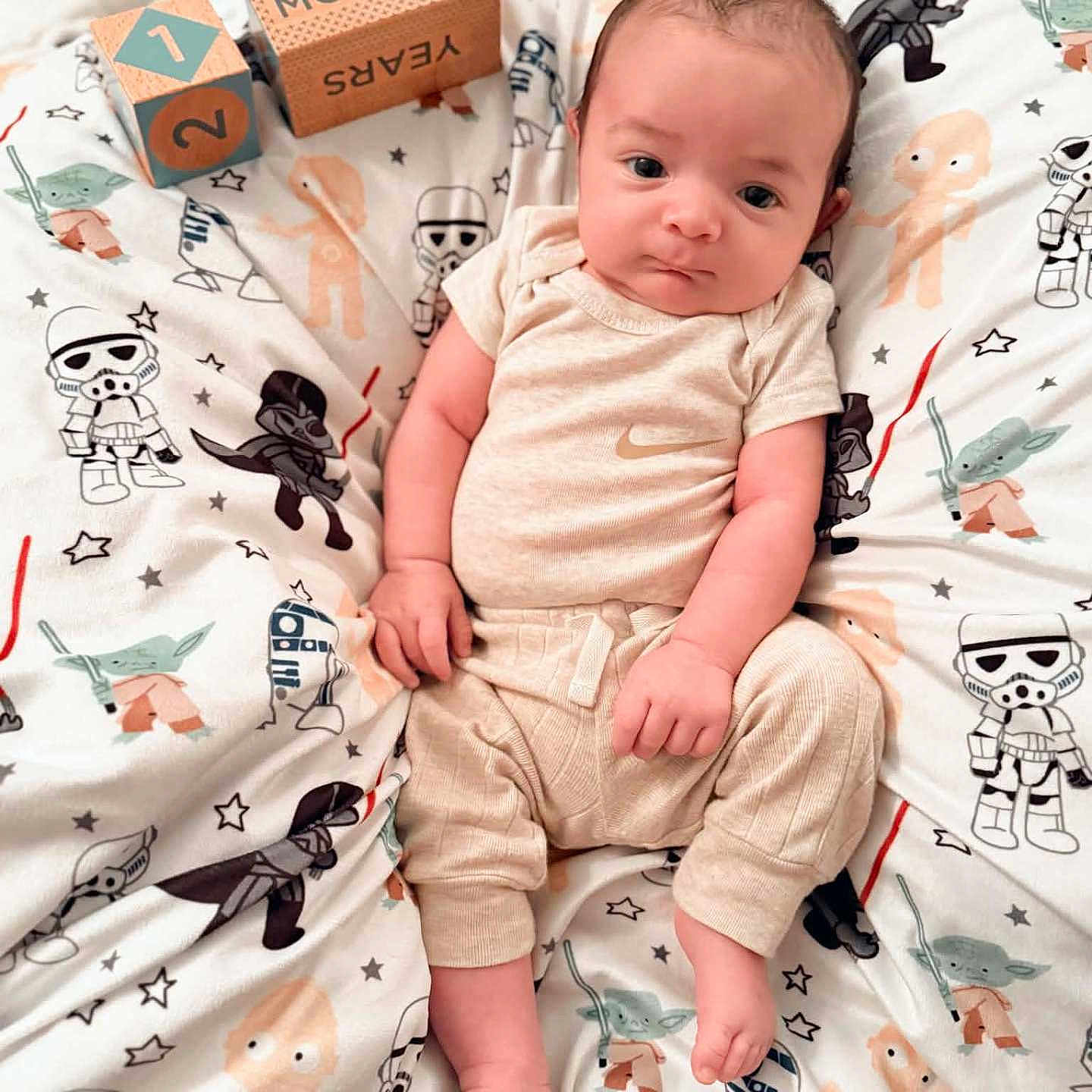 Exton is registered to the contest to win money with this photo: alien, baby, bedding, beige_clothing, blanket, bodysuit, child, droid, eyes, face, family_photo, indoors, infant, lying_down, milestone_blocks, months, portrait, smiling, star_wars, stormtrooper