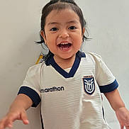 Mia joined the competition — help win amazing prizes! child, toddler, smiling, happy, sports_jersey, white_shirt, navy_trim, indoor, portrait, cute, person, short_hair, dark_hair, cheerful, young_child, face, front_view, casual_clothing, playing, joyful
